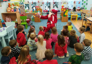 Dzieci siedzą na dywanie Mikołaj czyta świąteczną opowieść.